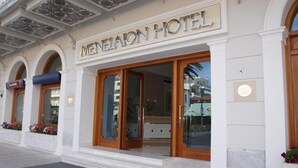 L'esterno dell'Hotel Menelaon, con ampie porte in vetro e un design architettonico classico.