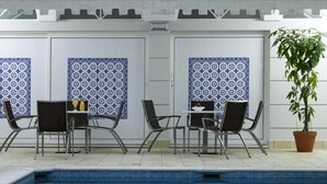 Area piscina con due tavoli e sedie, una pianta in vaso e piastrelle decorate.