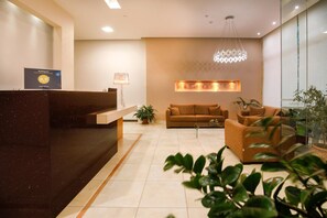 A hotel reception area with a reception desk, a sofa, a coffee table, and a chandelier. - Hotel Athina (Lamia)
