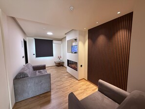 Un salon moderne avec un canapé gris, un plancher en bois, une cheminée et un téléviseur fixé au mur.