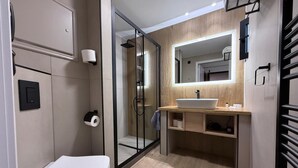 A modern bathroom with a toilet, a glass-enclosed shower, a sink with a mirror above it, and a towel rack. - Hotel Athina (Lamia)