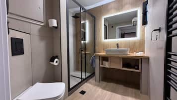 A modern bathroom with a toilet, a glass-enclosed shower, a sink with a mirror above it, and a towel rack.