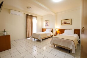 A hotel room with two beds, a desk, a chair, a potted plant, and a window with curtains. - Hotel Athina (Lamia)