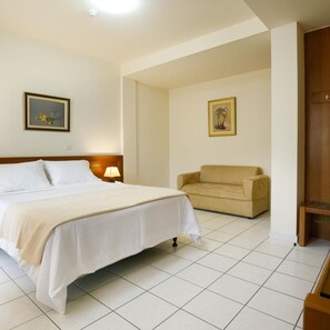 A hotel room with a bed, a sofa, a lamp, and two framed pictures on the walls. - Hotel Athina (Lamia)