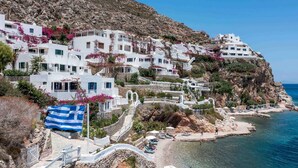 Un village côtier aux bâtiments blancs, adossé à une colline rocheuse et bordé par une mer d’un bleu limpide.