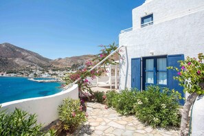 A white building with blue shutters, a stone pathway, and pink flowers.
