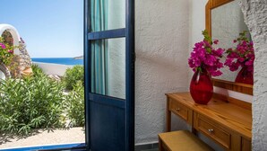 Une chambre avec vue sur la mer, une coiffeuse en bois avec un miroir et un vase rouge rempli de fleurs.