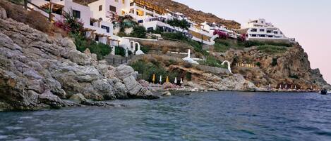 A coastal hotel with white buildings, rocky cliffs, and clear blue waters.
