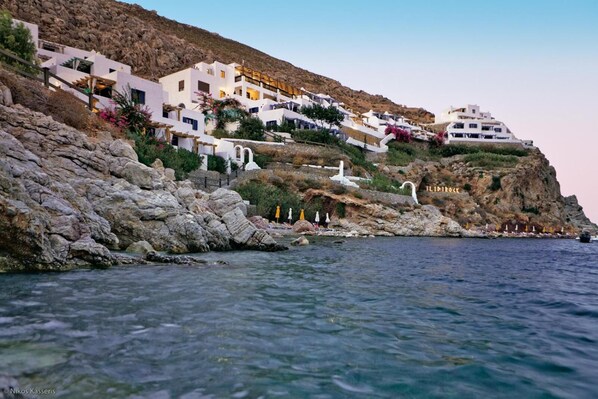 A coastal hotel with white buildings, rocky cliffs, and clear blue waters.