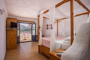 A bedroom with a wooden four-poster bed, a bedside table with a phone, and a view of a balcony with outdoor furniture.