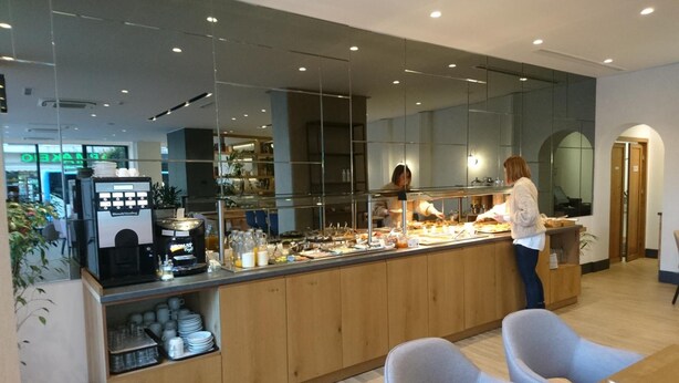 A modern cafe with a self-service counter, a coffee machine, and seating area with chairs and a table. - Park (Larissa)