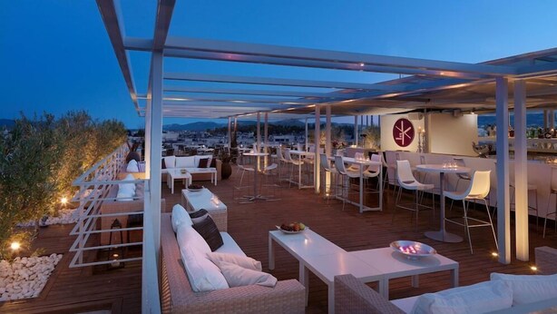 An outdoor terrace with seating, a bar area, and a view of the cityscape.