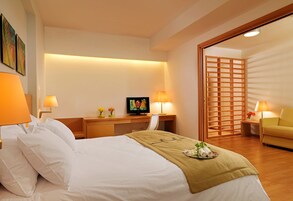 A hotel room with a bed, bedside tables, a desk with a television, and a sliding door leading to another room.