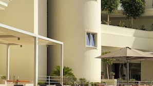 A poolside area with lounge chairs and umbrellas, a pool, and a building with balconies and plants.