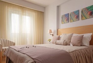 Una habitació d'hotel amb un llit gran, una cadira, una làmpada i tres quadres a la paret.