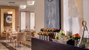 A modern hotel lobby with a reception desk, dining area, and artwork on the walls.