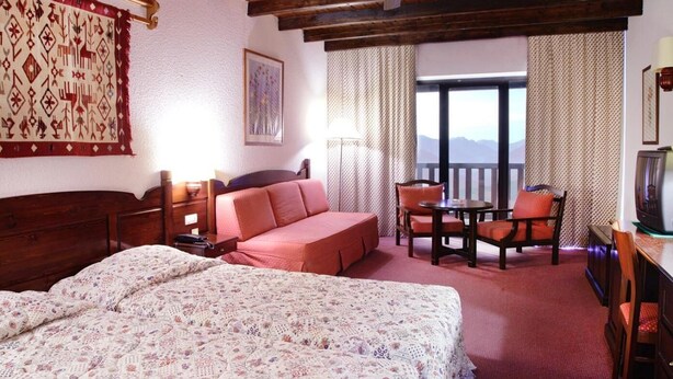 A hotel room with a large bed, a sofa, a dining table with chairs, a television, and a balcony with a view. - Montana Hotel Spa (Karpenisi)