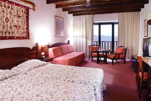 Ein Hotelzimmer mit einem großen Bett, einer Couch, einem Esstisch mit Stühlen, einem Fernseher und einem Balkon mit Blick.