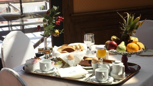 Bandeja de desayuno con pan, huevos, fruta y bebidas sobre una mesa con vistas al exterior.