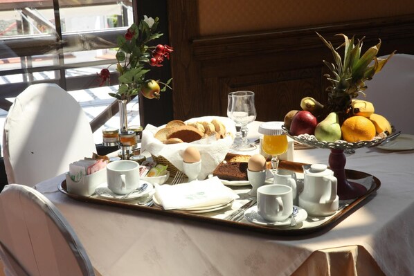 A breakfast tray with bread, eggs, fruit, and beverages on a table with a view of the outdoors. - Montana Hotel Spa (Karpenisi)