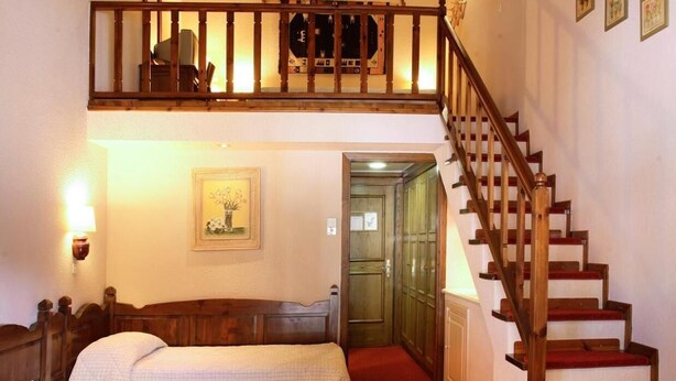 Quarto de hotel com duas camas, escada de madeira, uma pequena mesa e um ventilador de teto.