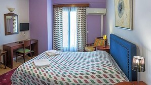 A hotel room with a bed, a desk, a chair, a lamp, and a window with curtains. - City Hotel Apollonion (Karpenisi)