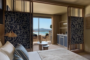 Habitación de hotel con cama, una mesita, una silla, vista al océano y kitchenette.