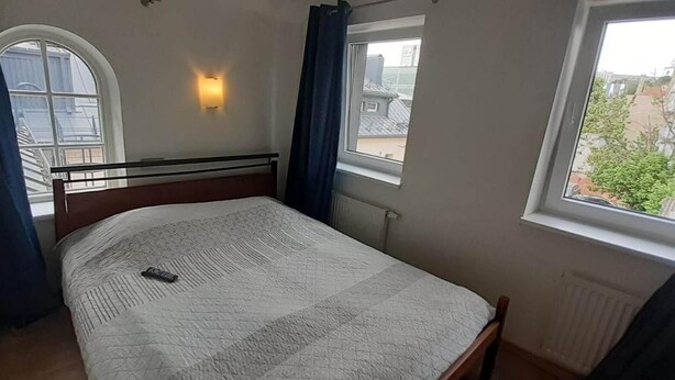 Une chambre à coucher avec un lit, deux fenêtres et un luminaire fixé au mur.