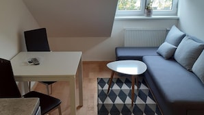 Un appartement moderne de style « loft » comprenant un coin repas, un canapé, une petite table ronde et une fenêtre avec des stores.