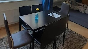 Une petite pièce moderne, dotée d’une table à manger, de chaises, d’un vase bleu et d’une grande fenêtre.