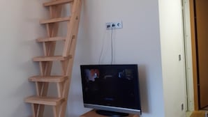Une pièce avec un escalier en bois, un téléviseur posé sur un meuble en bois et une porte blanche à l’arrière-plan.
