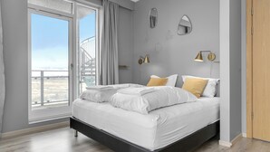 A modern bedroom with a large bed, a balcony, and a view of the city. - Icelandic Apartments (Kópavogur)