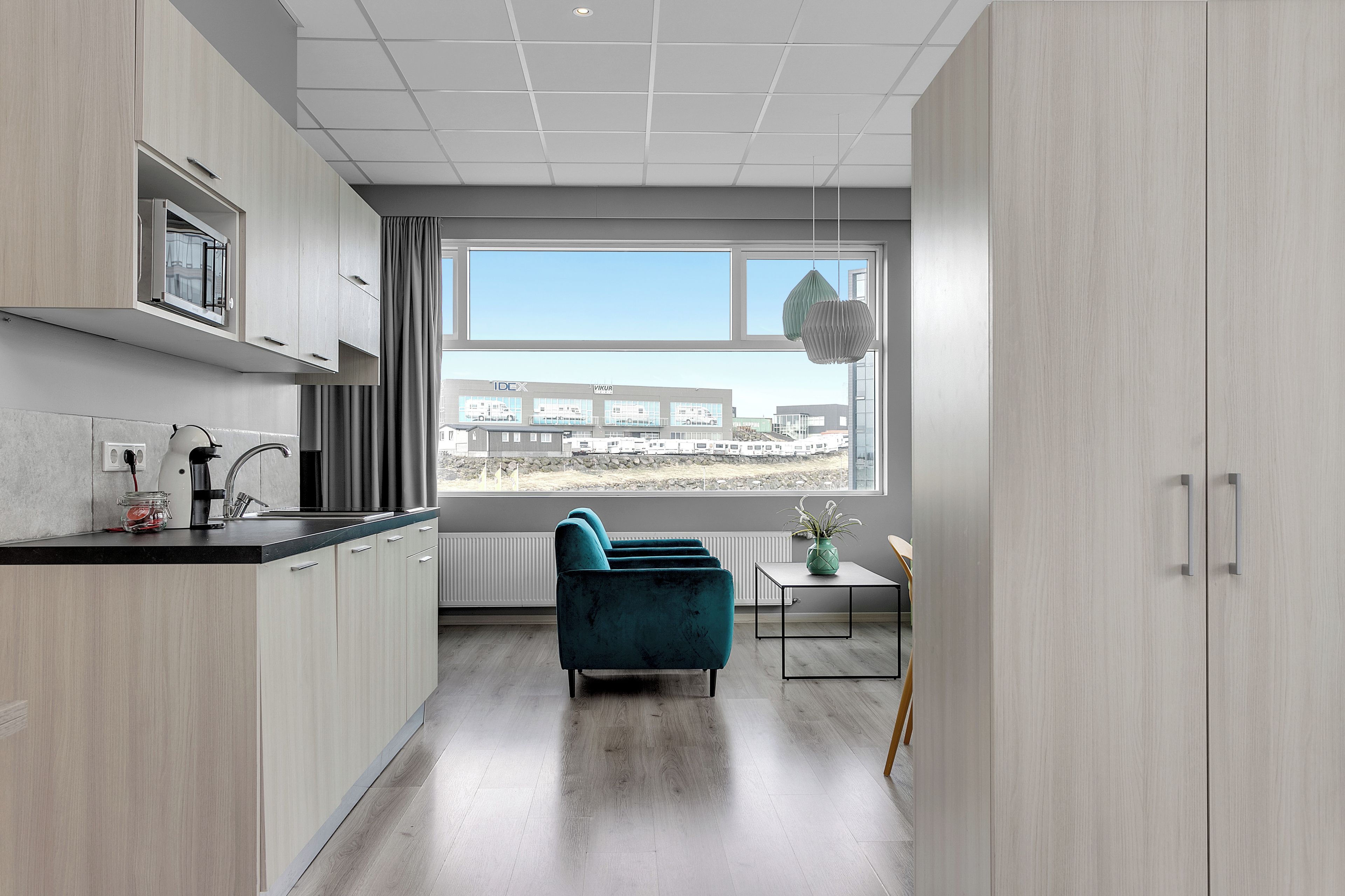 A modern kitchen with a built-in oven, a window with a view of a building, and a teal sofa in the living area.