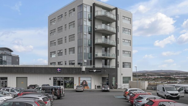 A multi-story building with a parking lot in front, featuring a sign for 'Outlets.' - Icelandic Apartments (Kópavogur)