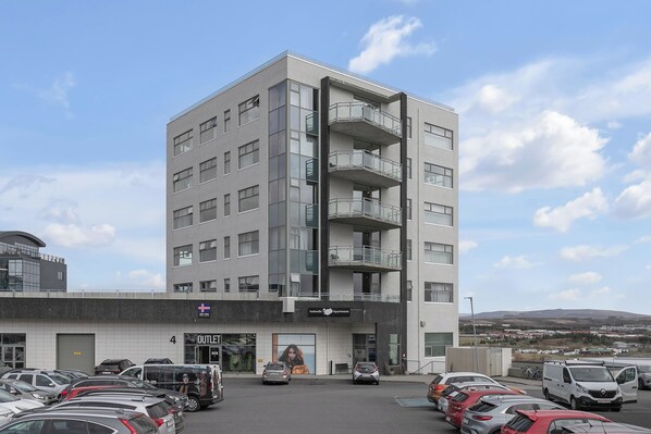 A multi-story building with a parking lot in front, featuring a sign for 'Outlets.' - Icelandic Apartments (Kópavogur)
