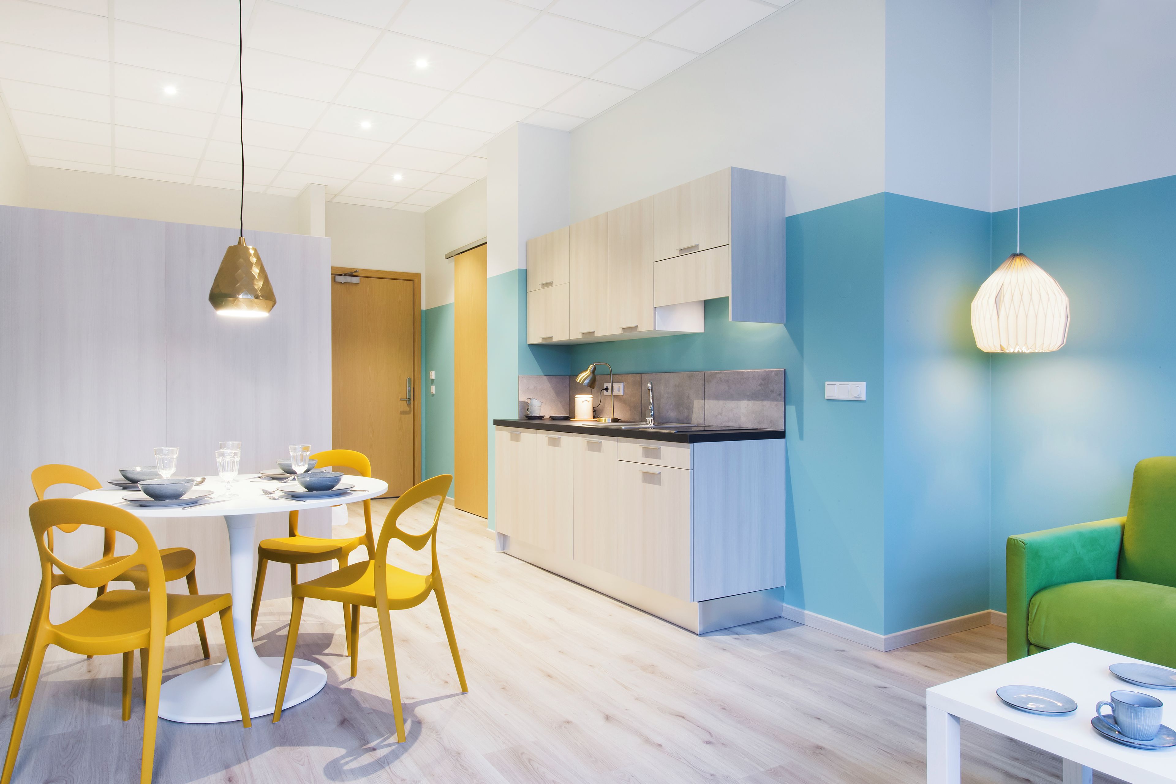 Una cocina moderna con armarios de madera clara, una isla central y una zona de comedor con sillas amarillas y una mesa blanca.