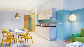 Una cocina moderna con armarios de madera clara, una isla central y una zona de comedor con sillas amarillas y una mesa blanca.