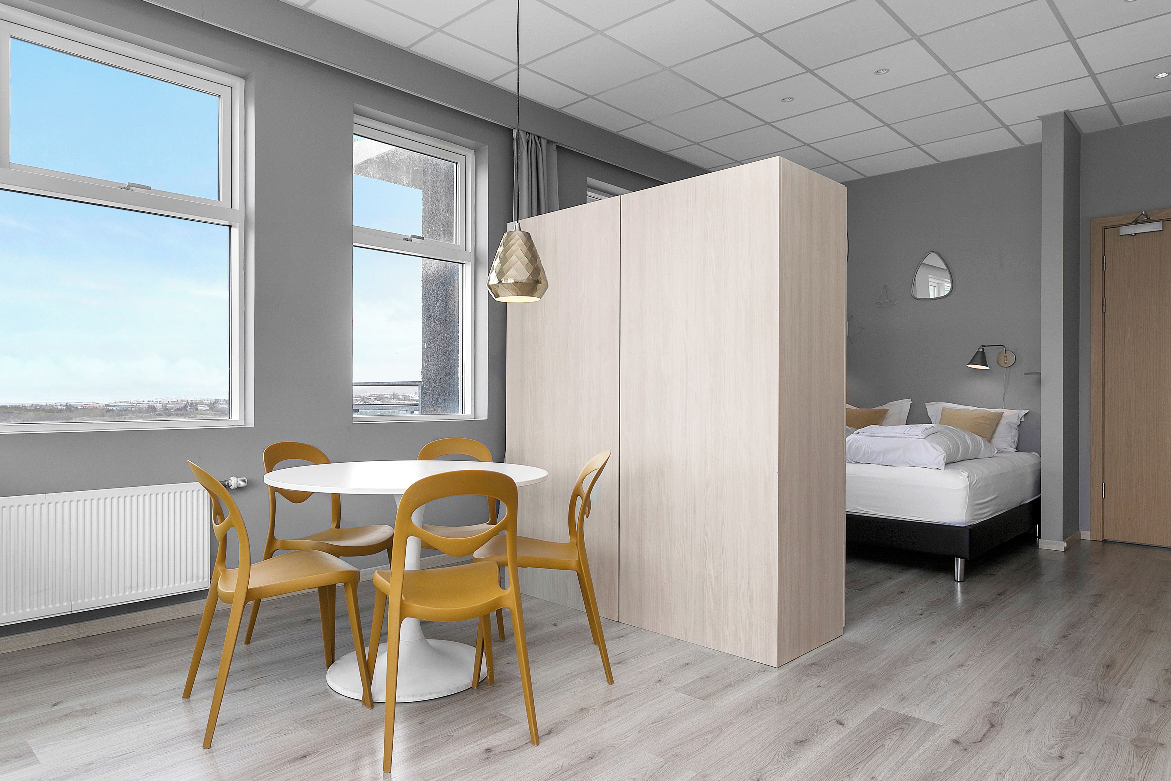A modern room with a round table and chairs, a bed, and a view through large windows.