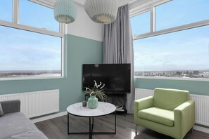 Una sala de estar moderna con un televisor grande, una mesa de centro redonda y un sillón verde.