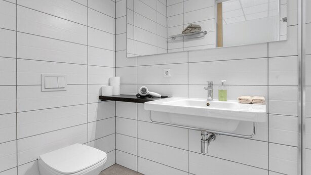 A modern bathroom with white tiles, a white sink, a toilet, and a towel rack. - Icelandic Apartments (Kópavogur)
