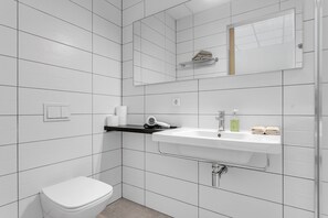 Moderni kylpyhuone, jossa on valkoiset laatat, valkoinen pesuallas, wc ja pyyhekoukku.