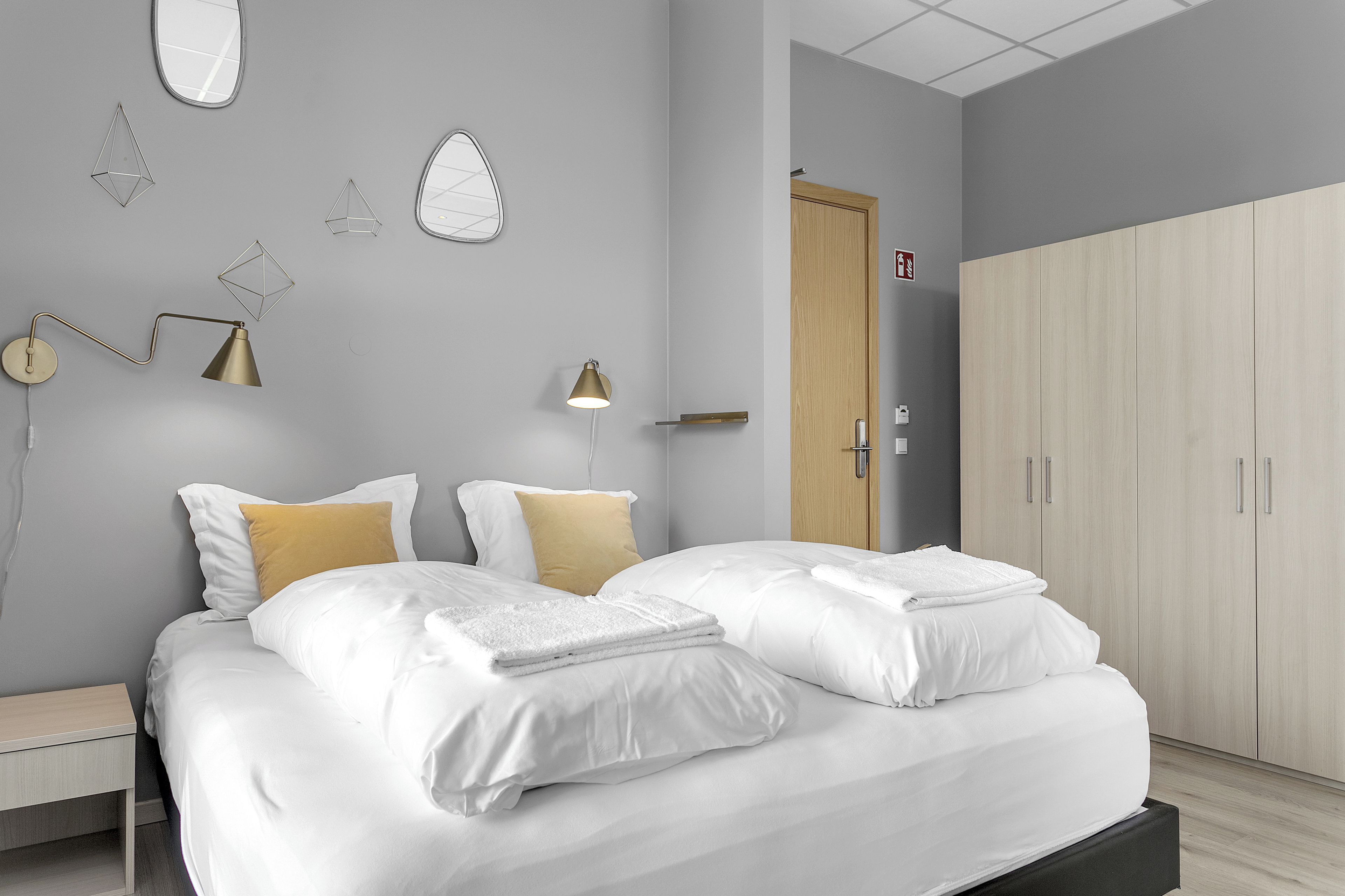 A modern bedroom with a bed, bedside tables, a wardrobe, and wall-mounted lamps.