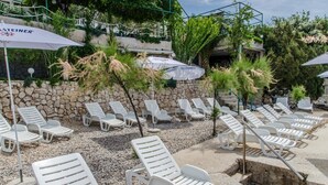 A row of white lounge chairs and umbrellas in a garden area with a stone wall and greenery. - Hotel Porat (Neum)