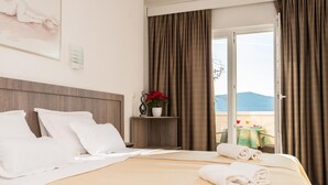 A hotel room with a bed, a nightstand with a vase of flowers, a window with curtains, and a view of the outdoors. - Hotel Porat (Neum)