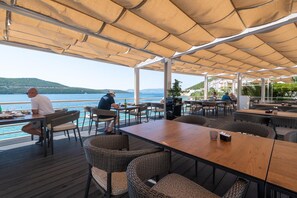 An outdoor dining area with tables and chairs, overlooking a body of water and hills. - Hotel Porat (Neum)