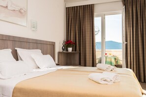 A hotel room with a bed, a nightstand with a vase of flowers, a window with curtains, and a view of the outdoors. - Hotel Porat (Neum)