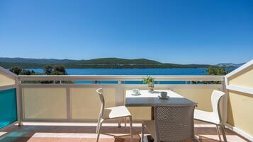 A balcony with a table and chairs, overlooking a body of water and distant hills.