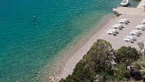 A coastal area with clear turquoise water, a pebble beach, and a row of white beach chairs. - Hotel Porat (Neum)