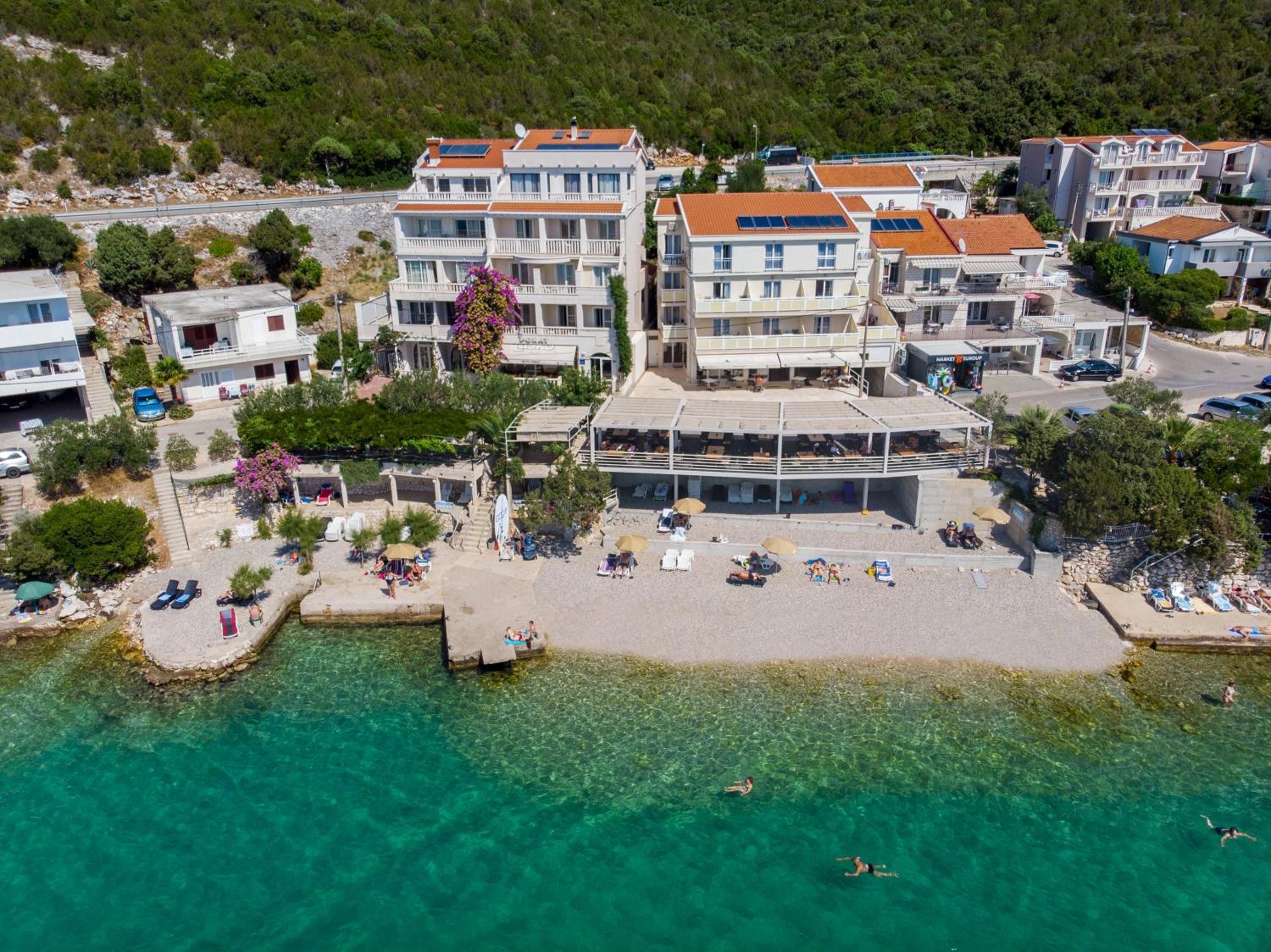 Eine Küstenstadt mit mehrstöckigen Gebäuden, einem Strand mit Liegestühlen und klarem türkisblauem Wasser.