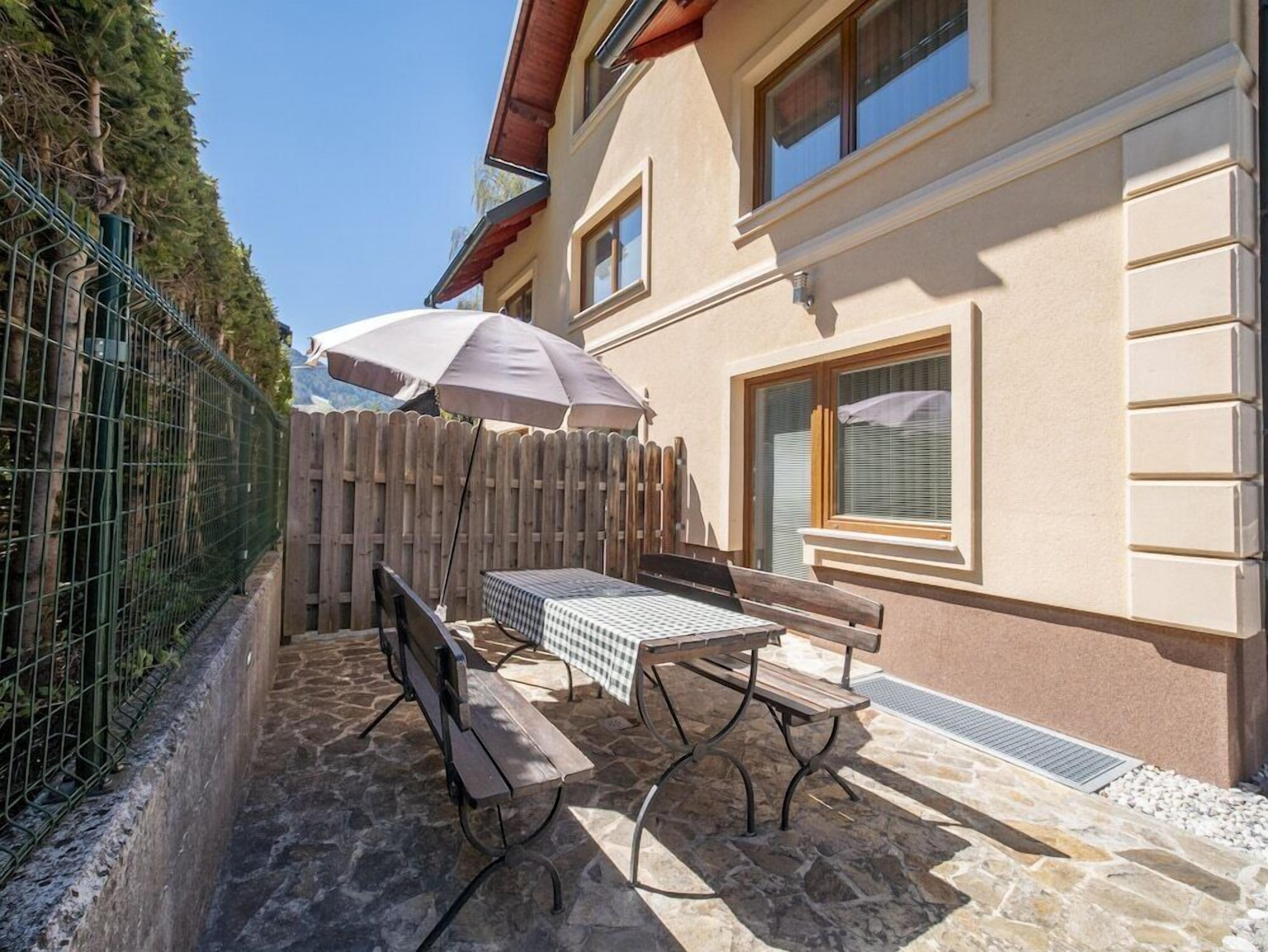 Eine Außenpatio mit Tisch und Bänken, einem Holzzaun und einem Gebäude mit Fenstern.